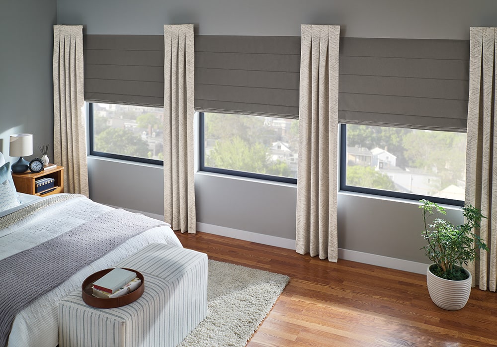 Master bedroom with layered shades and drapes on the windows filtering in light.